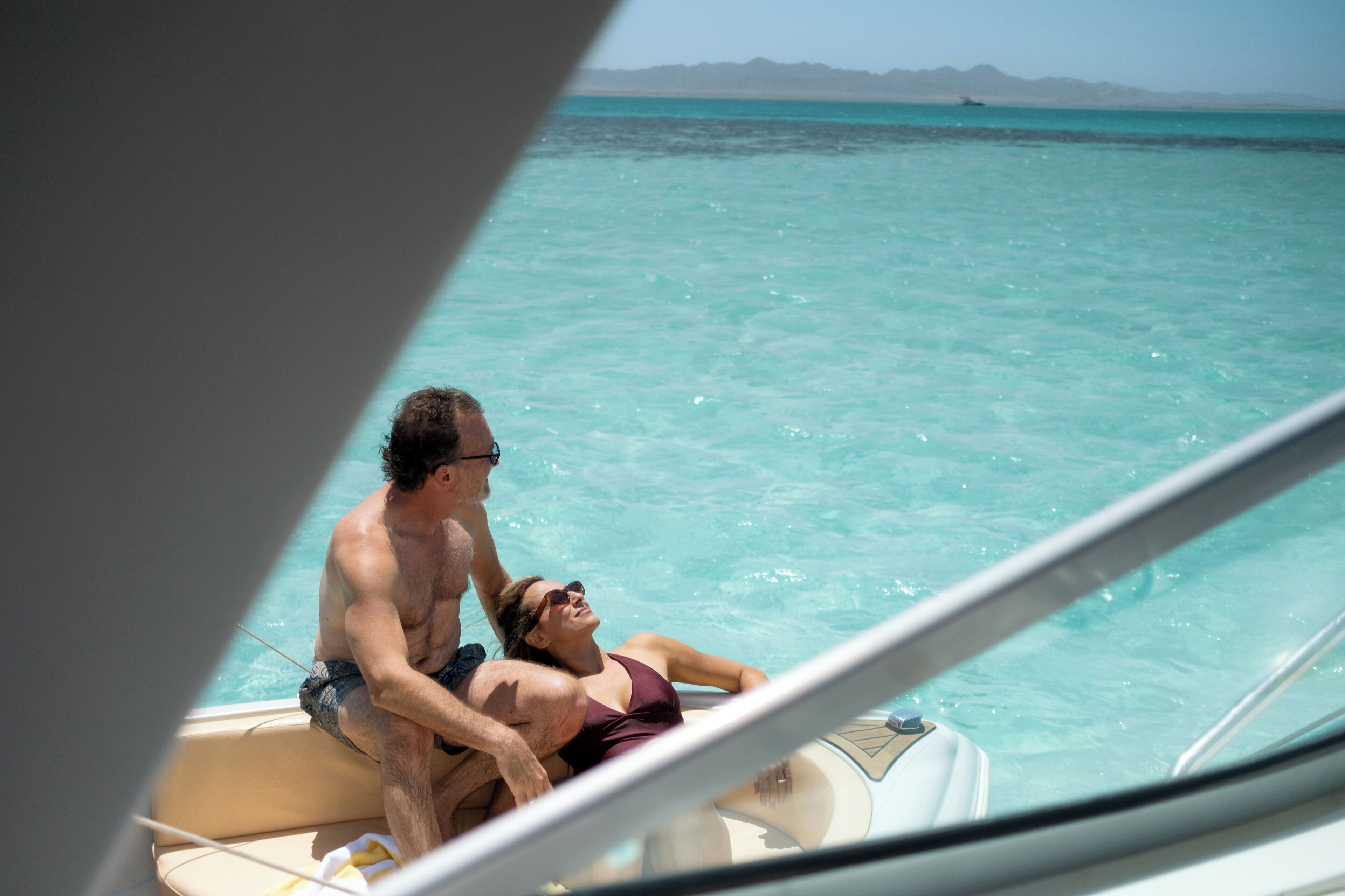 A boat with two people, one sitting and one standing, in clear turquoise water.