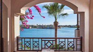 Un balcón con vistas a una masa de agua, una palmera y flores rosadas.