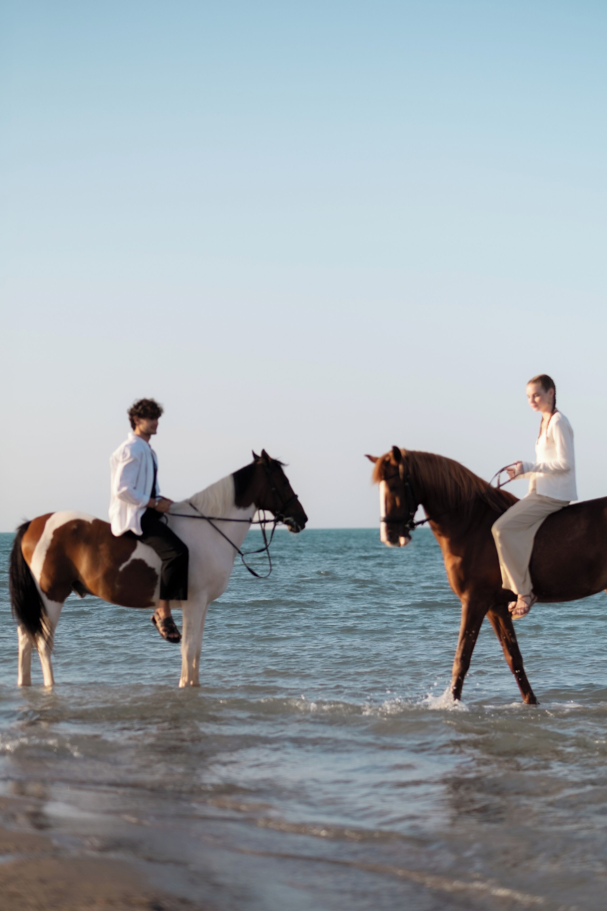 Twee personen rijden op paarden aan een strand, met de oceaan op de achtergrond.