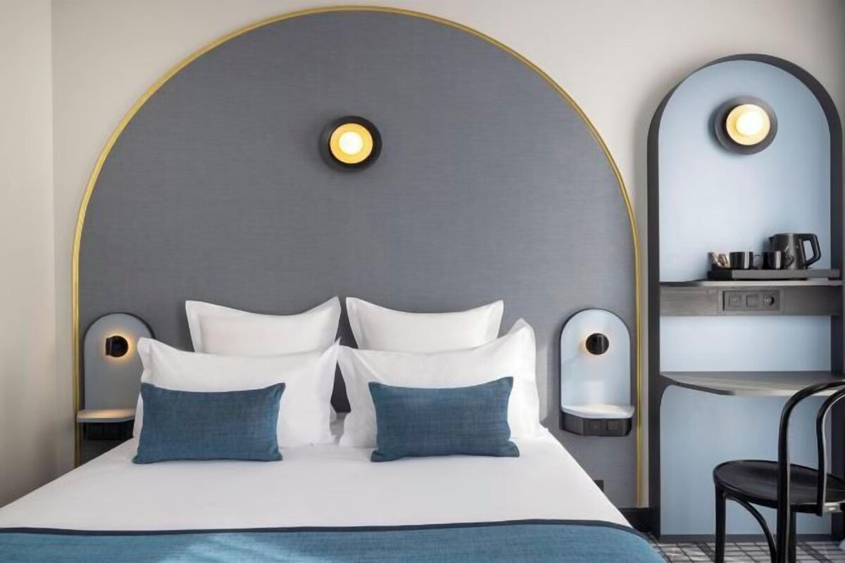 A modern hotel room with a large bed, two bedside tables, a built-in shelf, and a curved wall design.