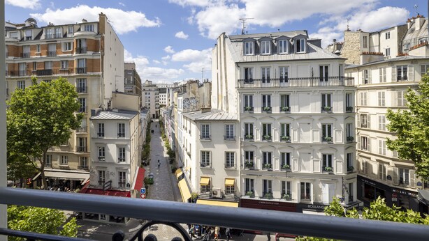 Una hilera de edificios históricos con balcones, una calle adoquinada y un cielo azul despejado.