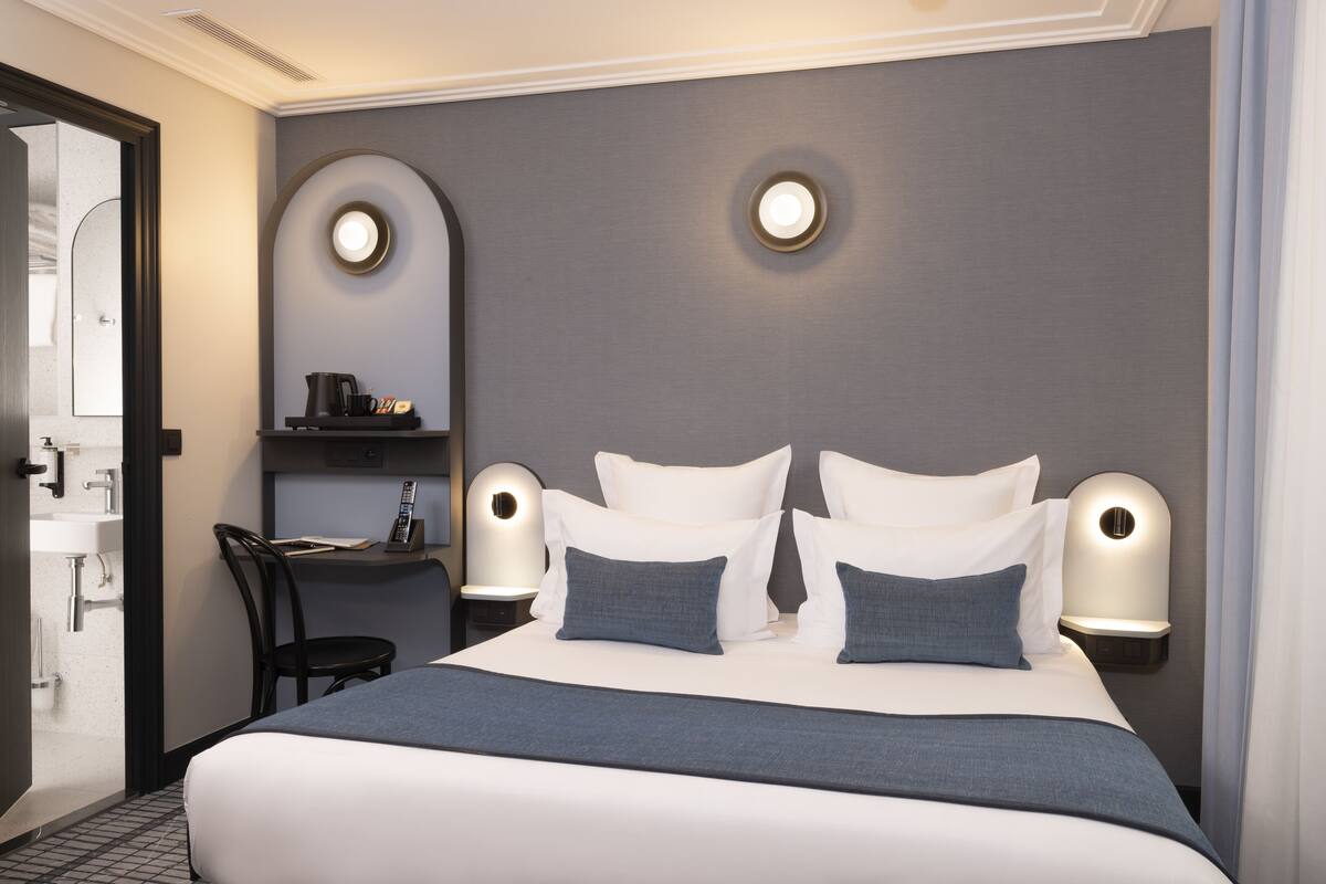 Ein modernes Hotelzimmer mit einem großen Bett, zwei Nachttischen mit Lampen, einem Sessel und einem kleinen Schreibtisch mit einer Lampe.