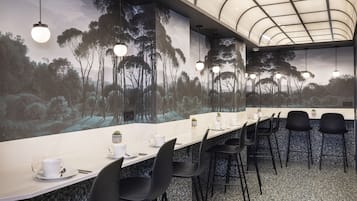 A long conference table with black chairs, a white tablecloth, and a mural of trees on the wall behind.