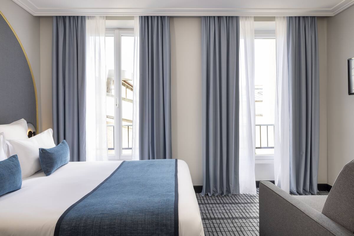 Ein Hotelzimmer mit einem großen Bett, einer Couch und Blick ins Freie durch transparente Vorhänge.
