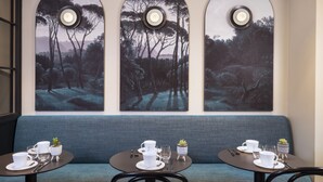 Un comedor con un sofá azul, dos mesas redondas y tres lámparas fijadas a la pared.