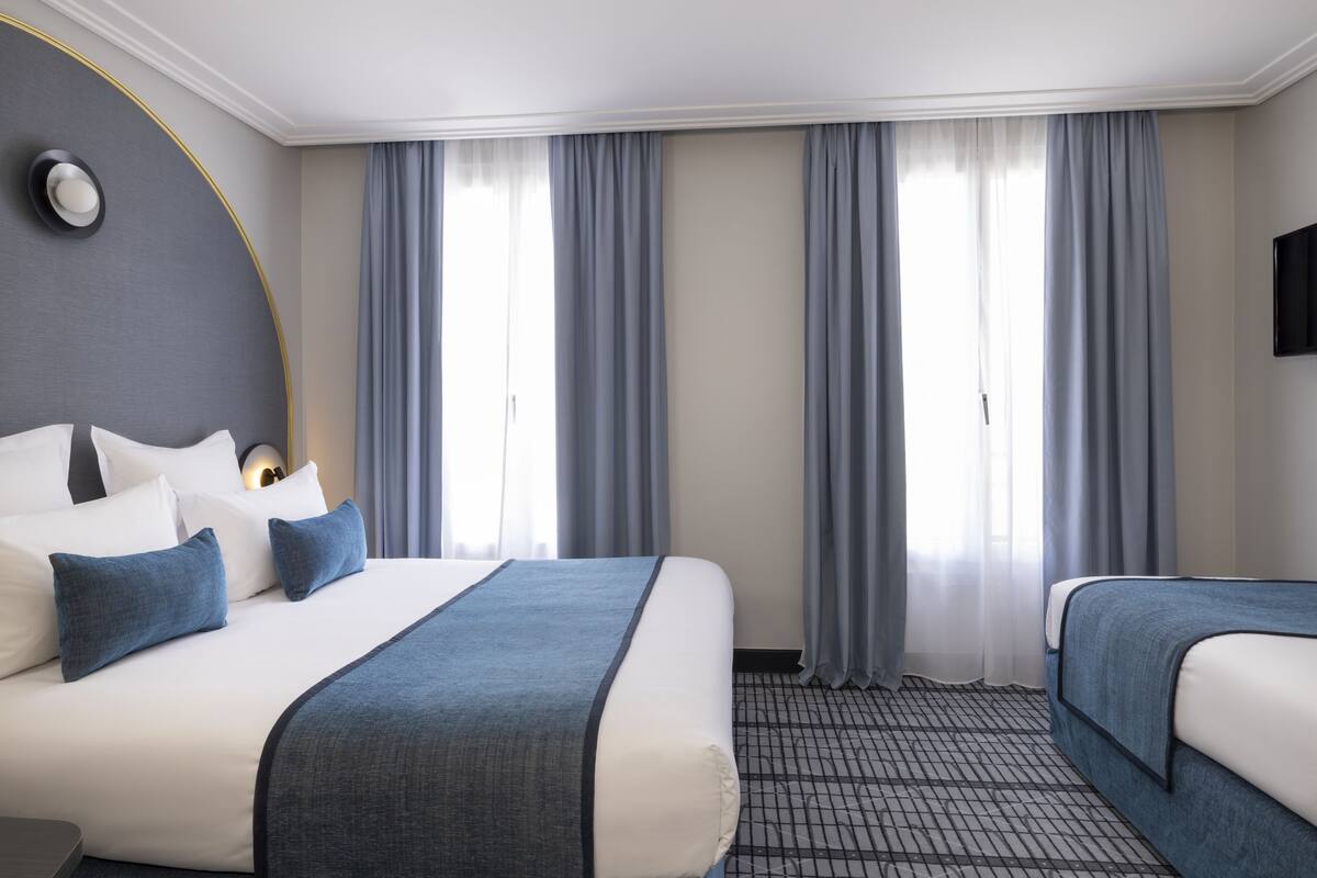Ein Hotelzimmer mit zwei Betten, einem großen Fenster mit Vorhängen, einem Flachbildfernseher und einem gemusterten Teppich.