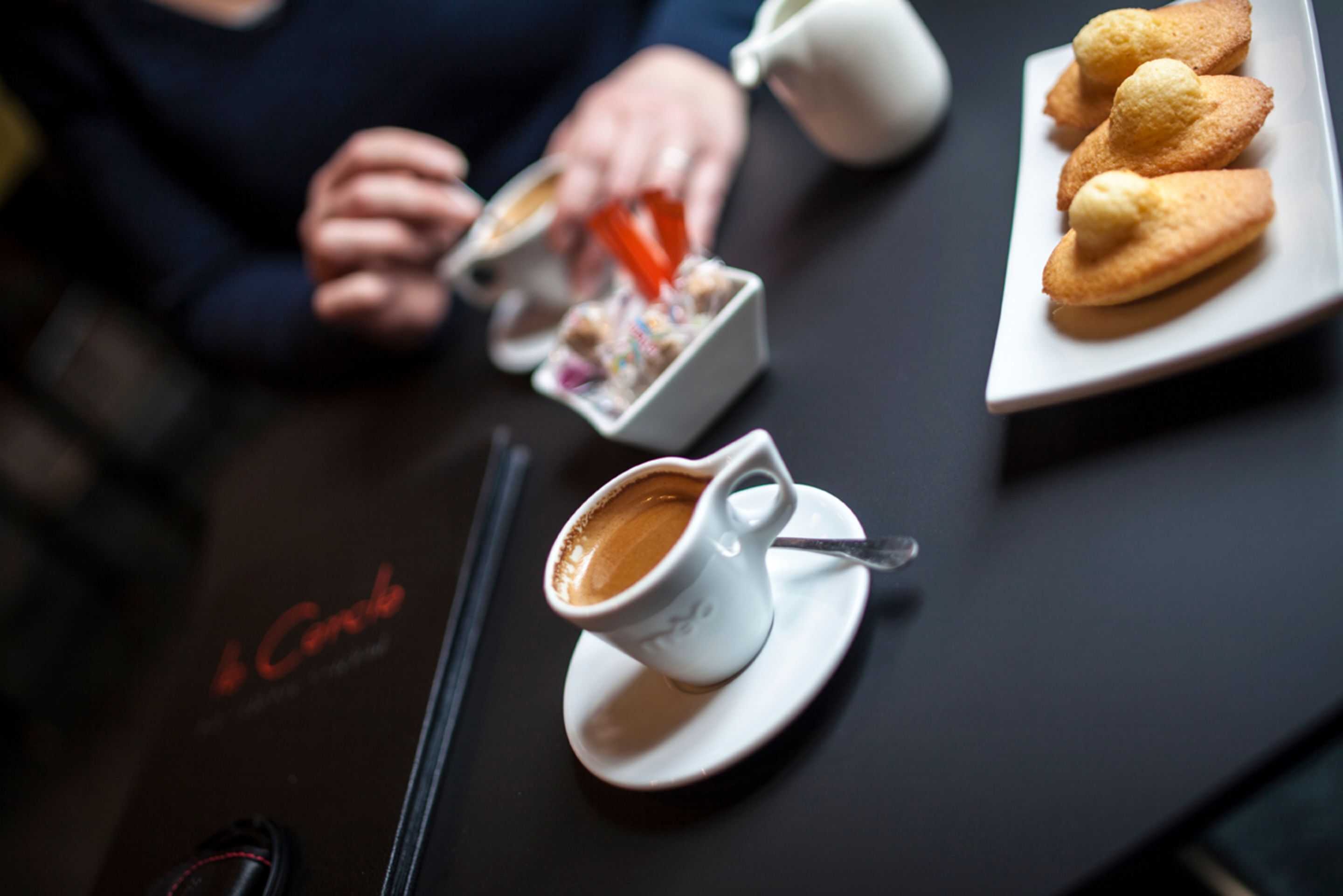 Une table avec une tasse de café, une assiette de pâtisseries et un petit récipient de sucre.