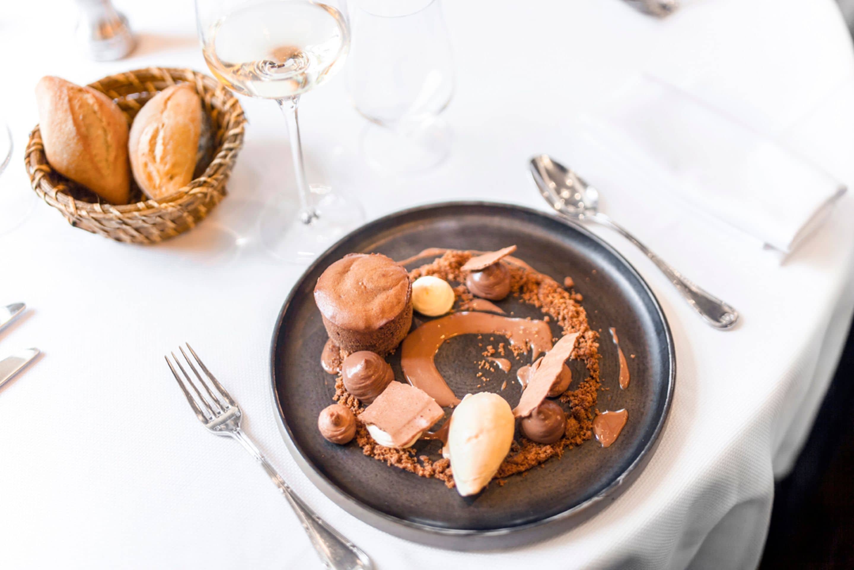 Ein Desserteller mit Schokoladenmousse, einer Kugel Eis und Schokoladenraspeln auf dunklem Unterteller.