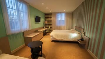 A hotel room with a bed, a desk, a chair, a small table, and a TV on the wall.