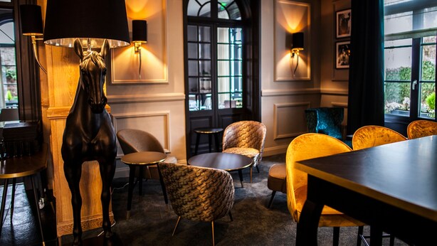 Een kamer met een grote tafel, meerdere stoelen, een beeld en wandlampen.