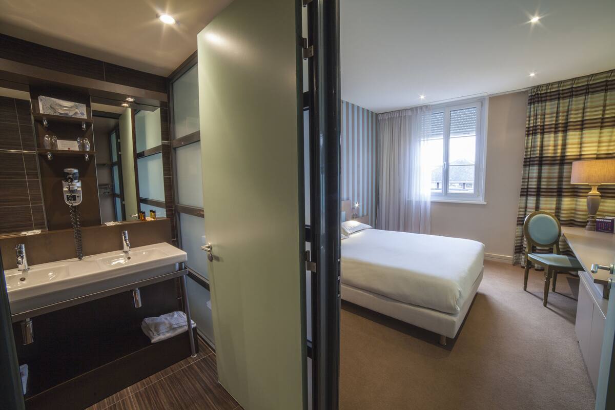 Ein Hotelzimmer mit Bad, Bett, Schreibtisch und Stuhl.