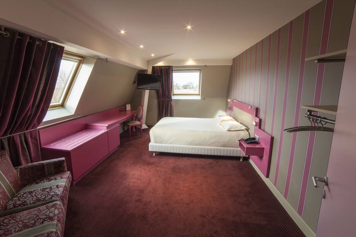 Ein Schlafzimmer mit einem Bett, einem Schreibtisch, einem Sessel, einem Fernseher und einem Fenster.