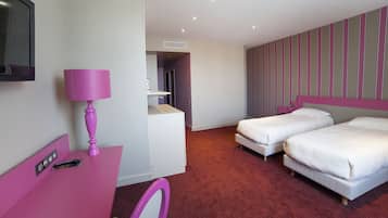 Habitación de hotel con dos camas, un escritorio con una lámpara rosa, televisión y pared a rayas.