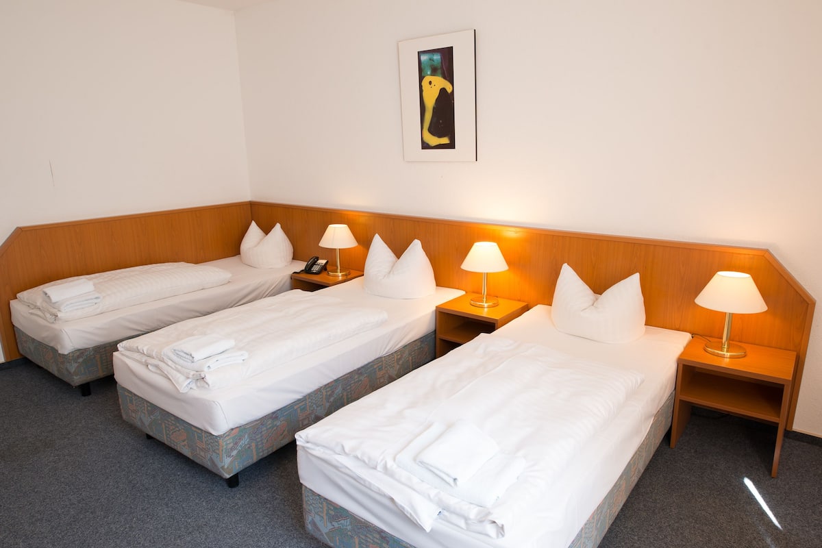 A hotel room with two single beds, each with a wooden headboard, white linens, and bedside lamps.