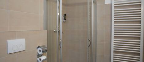 Een moderne badkamer met een douche met glazen wand, een toiletpapierautomaat en een handdoekhouder.