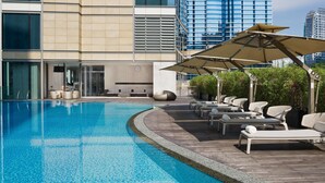 A modern pool area with lounge chairs and umbrellas, surrounded by a building with large windows and a view of other high-rise buildings. - EAST Hong Kong (Hong Kong)