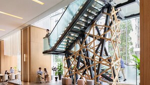 Ein modernes Interieur mit einer Glasstufenkonstruktion, Holzakzenten und einer Sitzecke mit Personen.