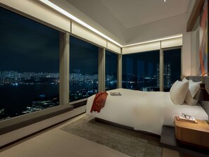 Ein modernes Hotelzimmer mit einem großen Bett, einem Nachttisch und Blick auf eine nächtliche Stadtansicht.
