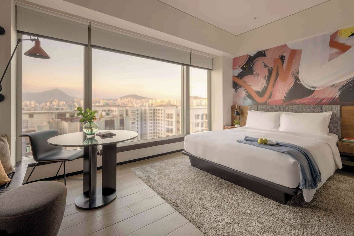A modern hotel room with a large bed, a round table, and a city view.