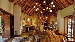 A spacious living area with a high ceiling, a central wooden table, a sofa, and a zebra rug.