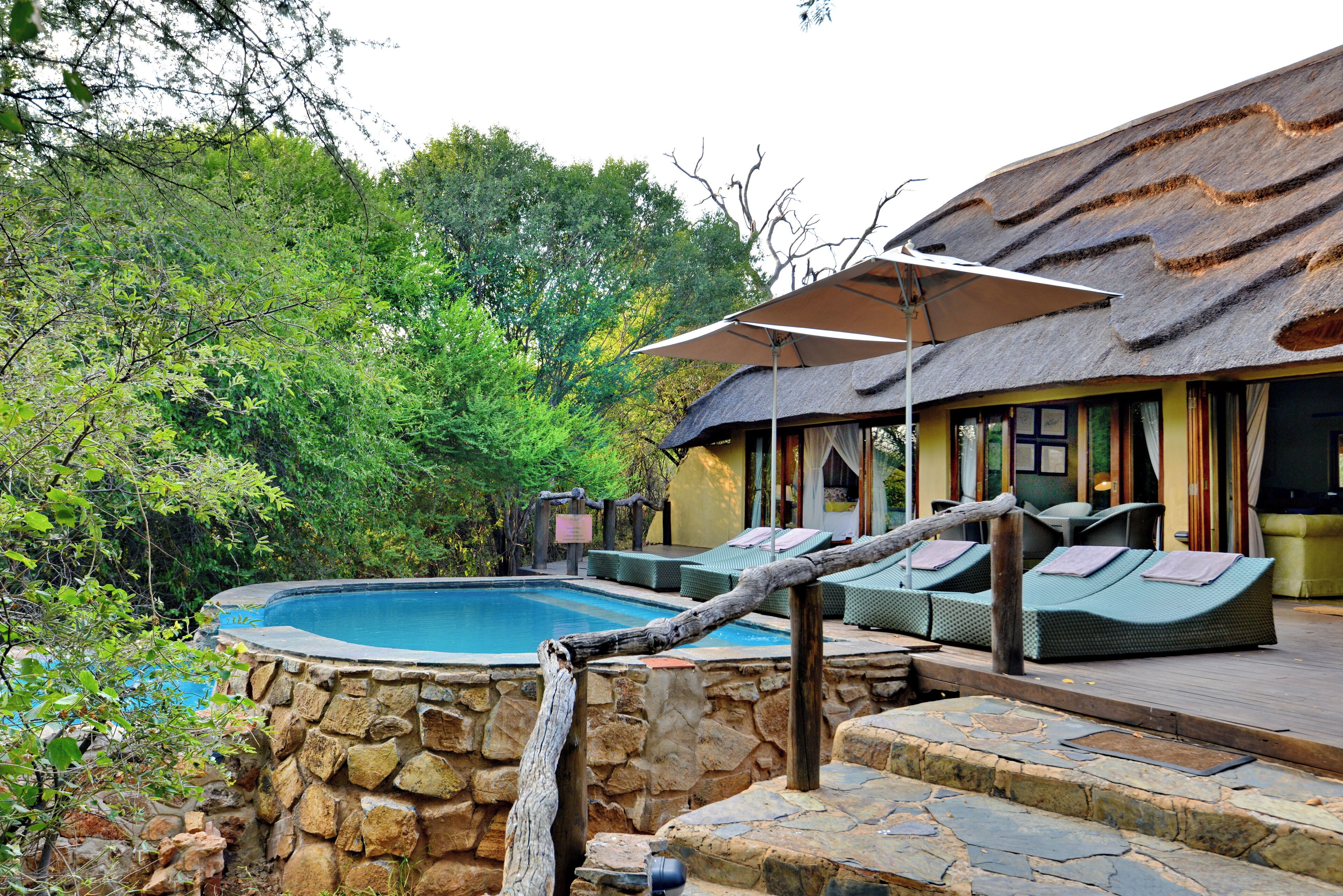 A pool area with stone walls, lounge chairs, and umbrellas.