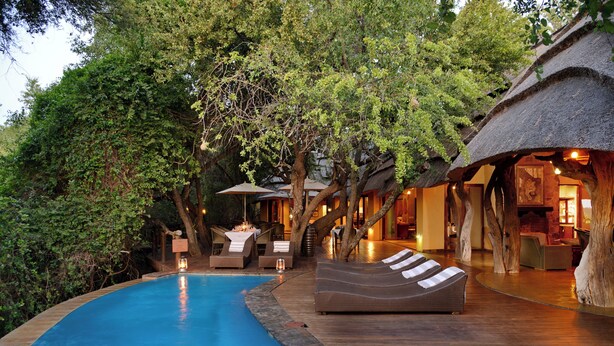 A poolside area with lounge chairs, a thatched-roof structure, and a wooden deck.