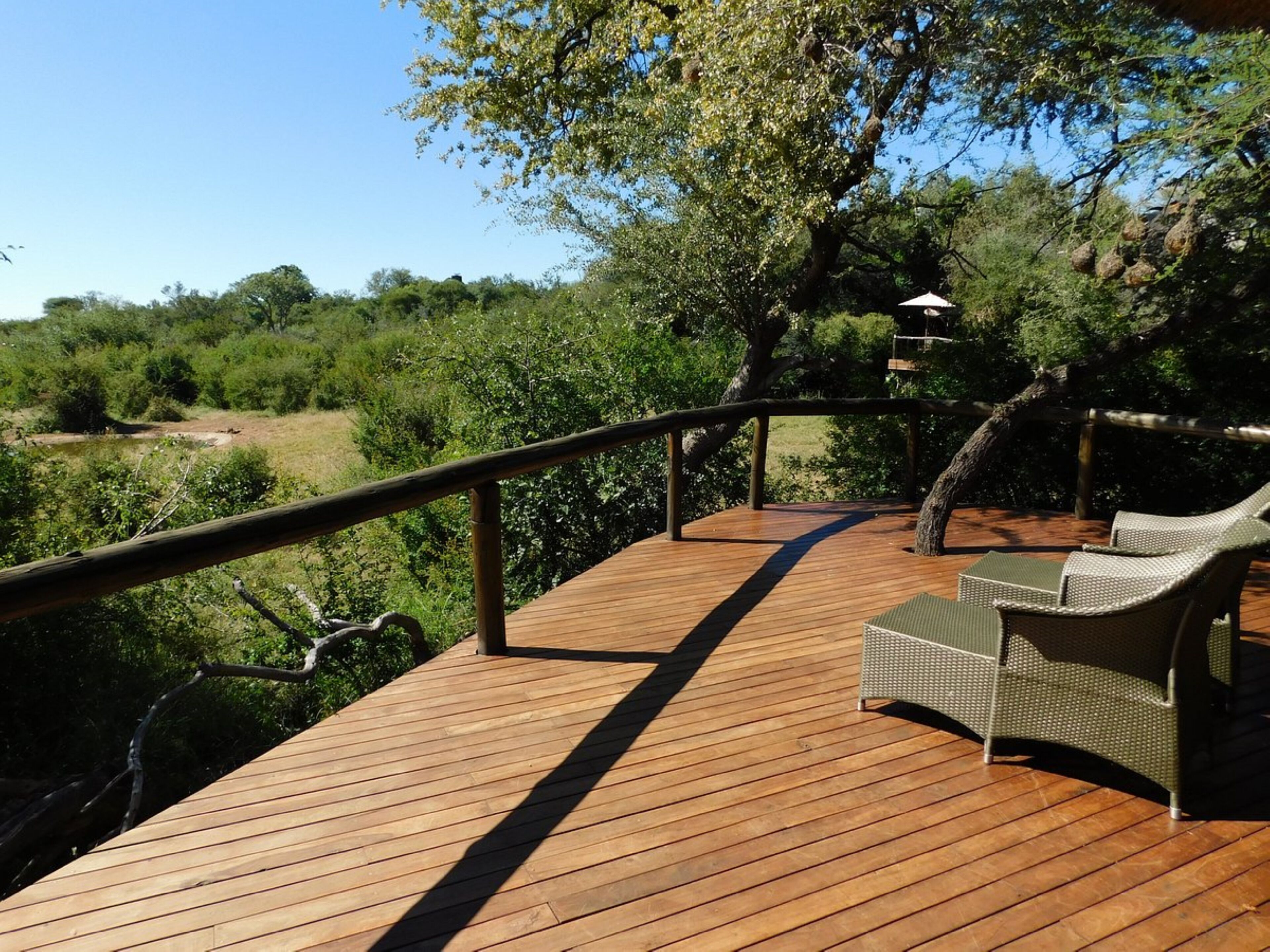 A wooden deck with a metal railing, two wicker lounge chairs, and a hanging light fixture.