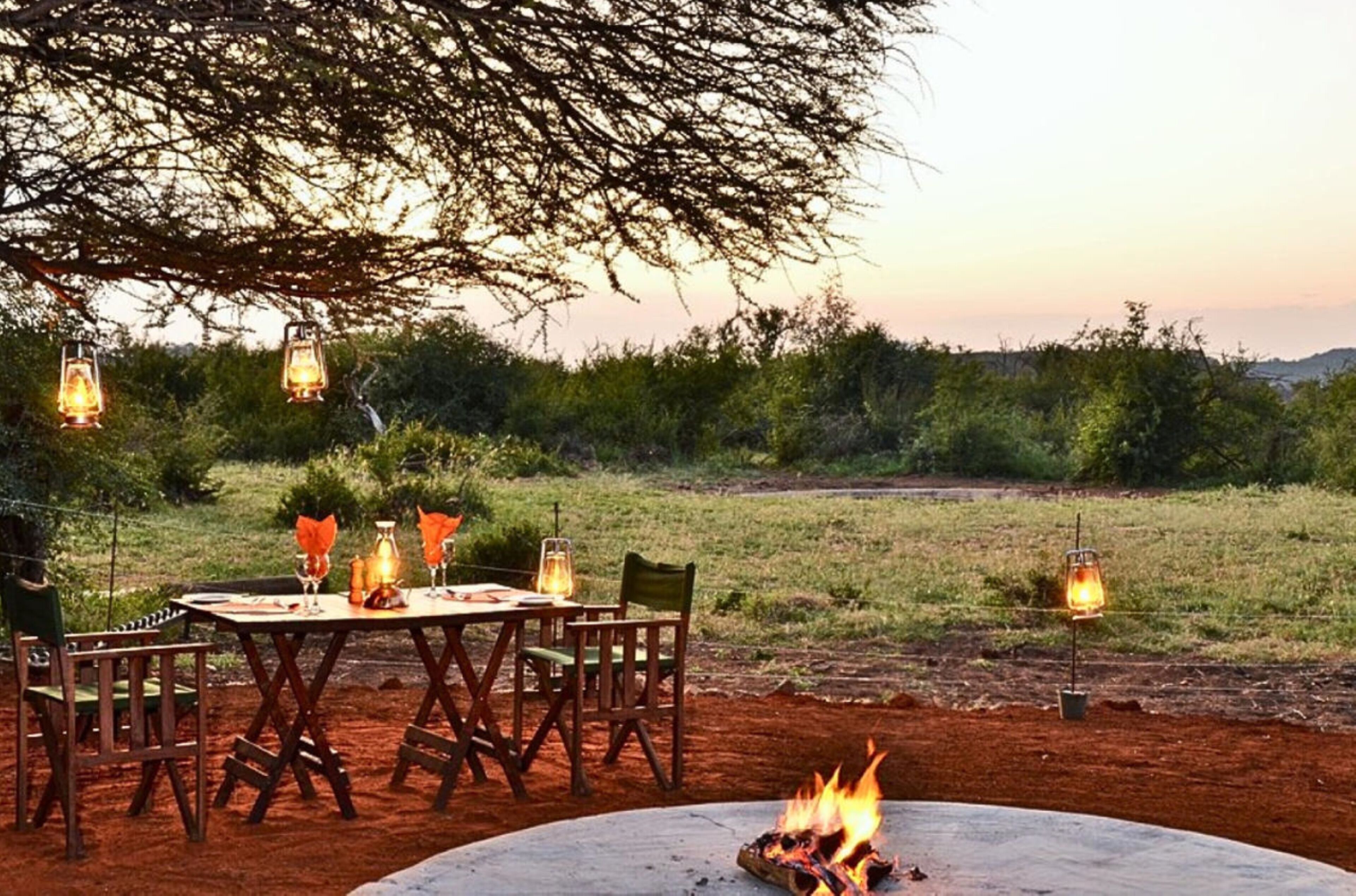 An outdoor dining area with a round table and chairs, surrounded by lanterns and a fire pit.