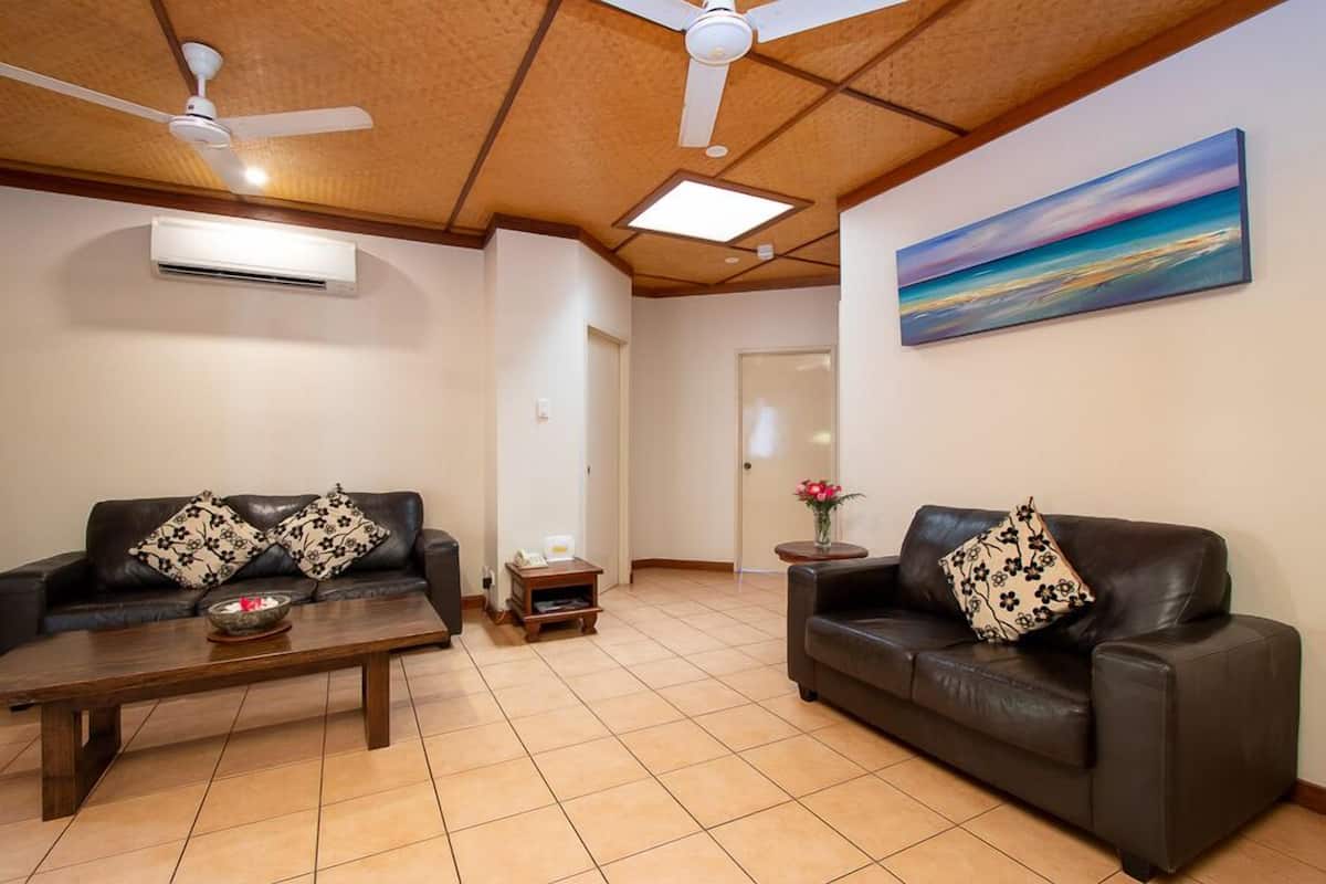 A living room with two leather sofas, a wooden coffee table, ceiling fans, and a painting on the wall.