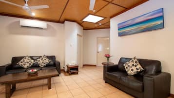 A living room with two leather sofas, a wooden coffee table, ceiling fans, and a painting on the wall.