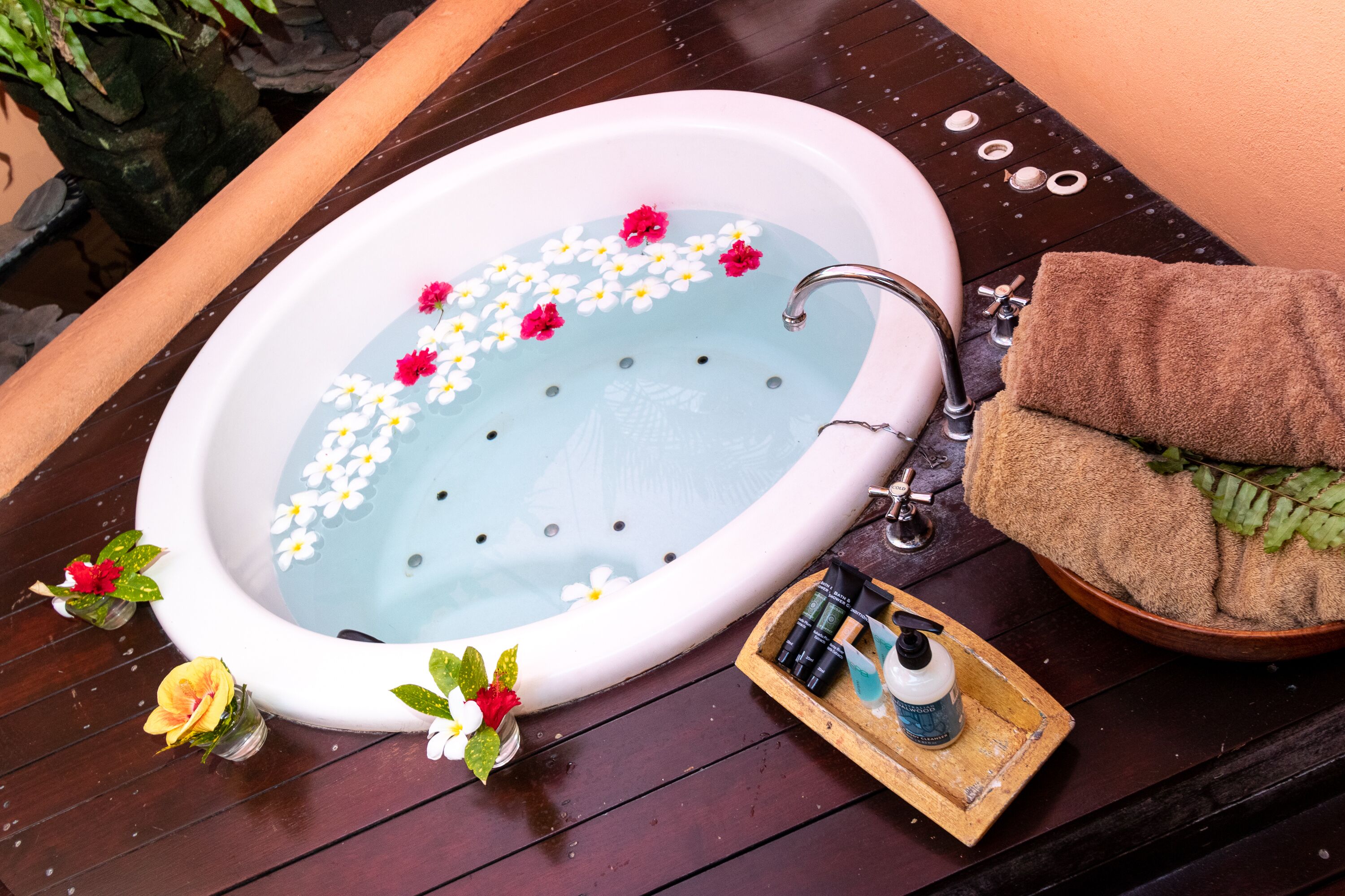 A bathtub with flowers, a towel, and toiletries on a wooden deck.