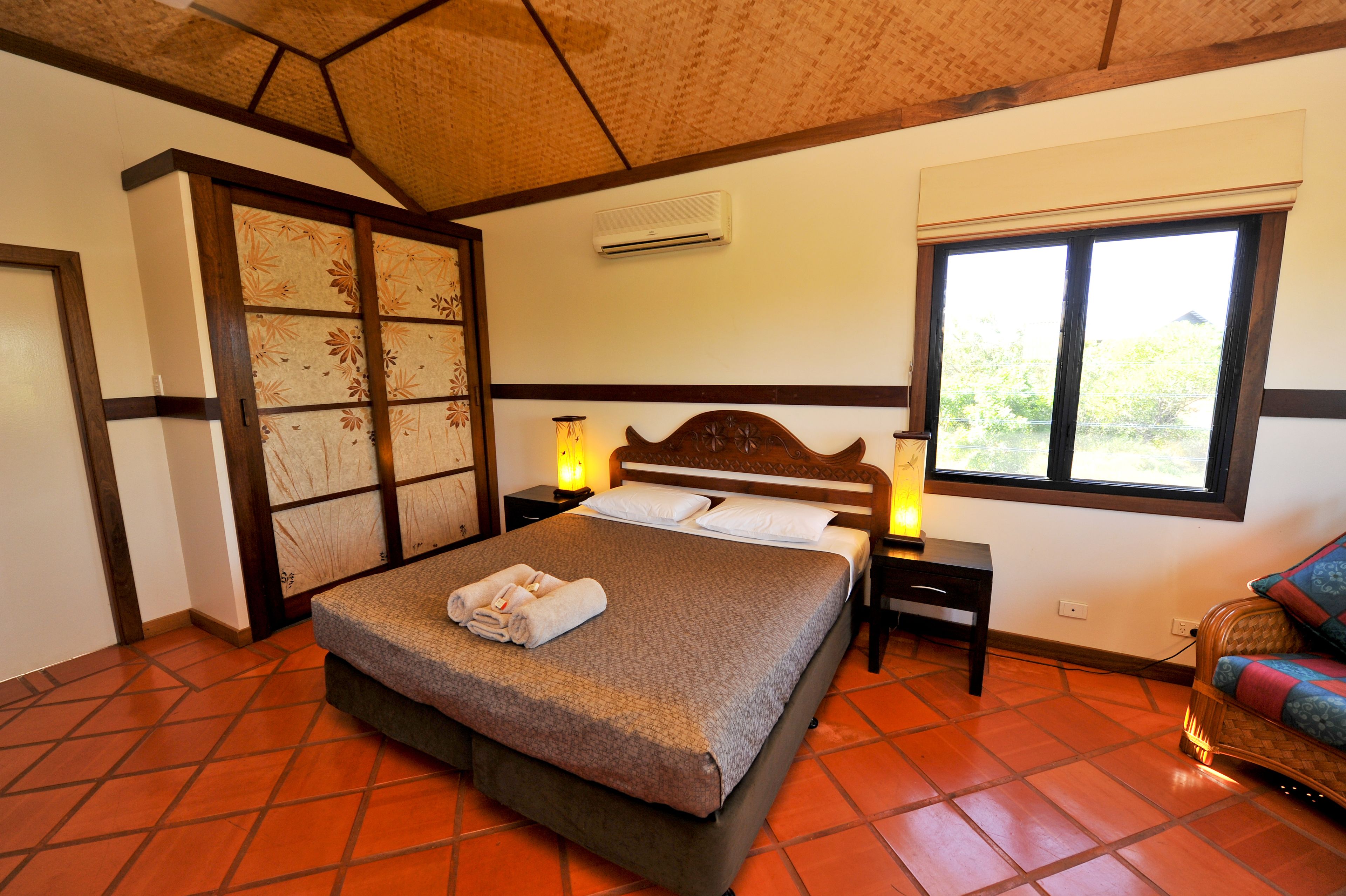 A hotel room with a bed, bedside lamps, a window, and a traditional Japanese-style wardrobe.