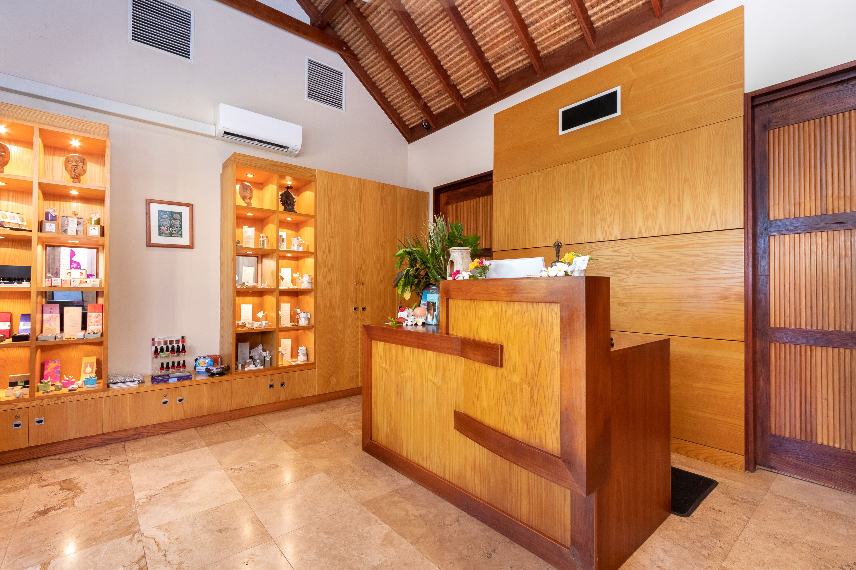 A reception area with wooden shelving displaying various items, a reception desk, and a large wooden door.