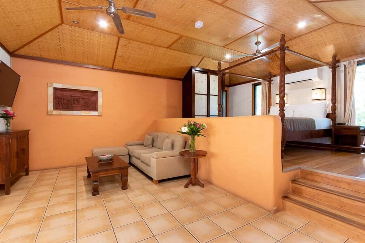 A room with a wooden ceiling, a four-poster bed, a sofa, a small table, and a vase of flowers.
