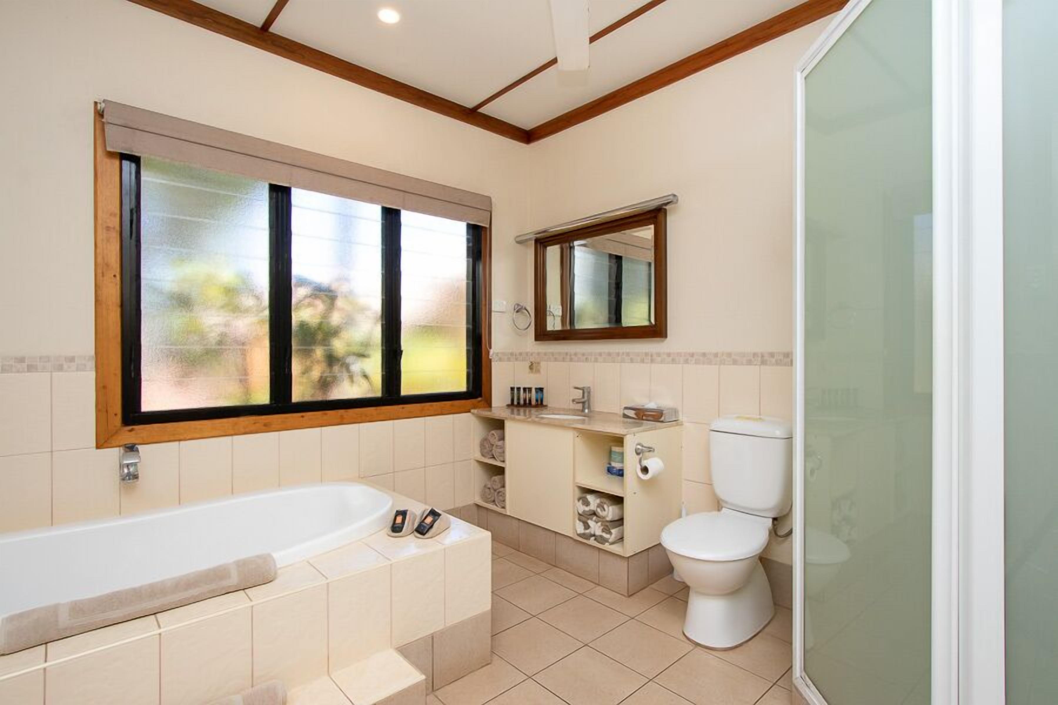 A modern bathroom with a bathtub, toilet, and a large window providing natural light.
