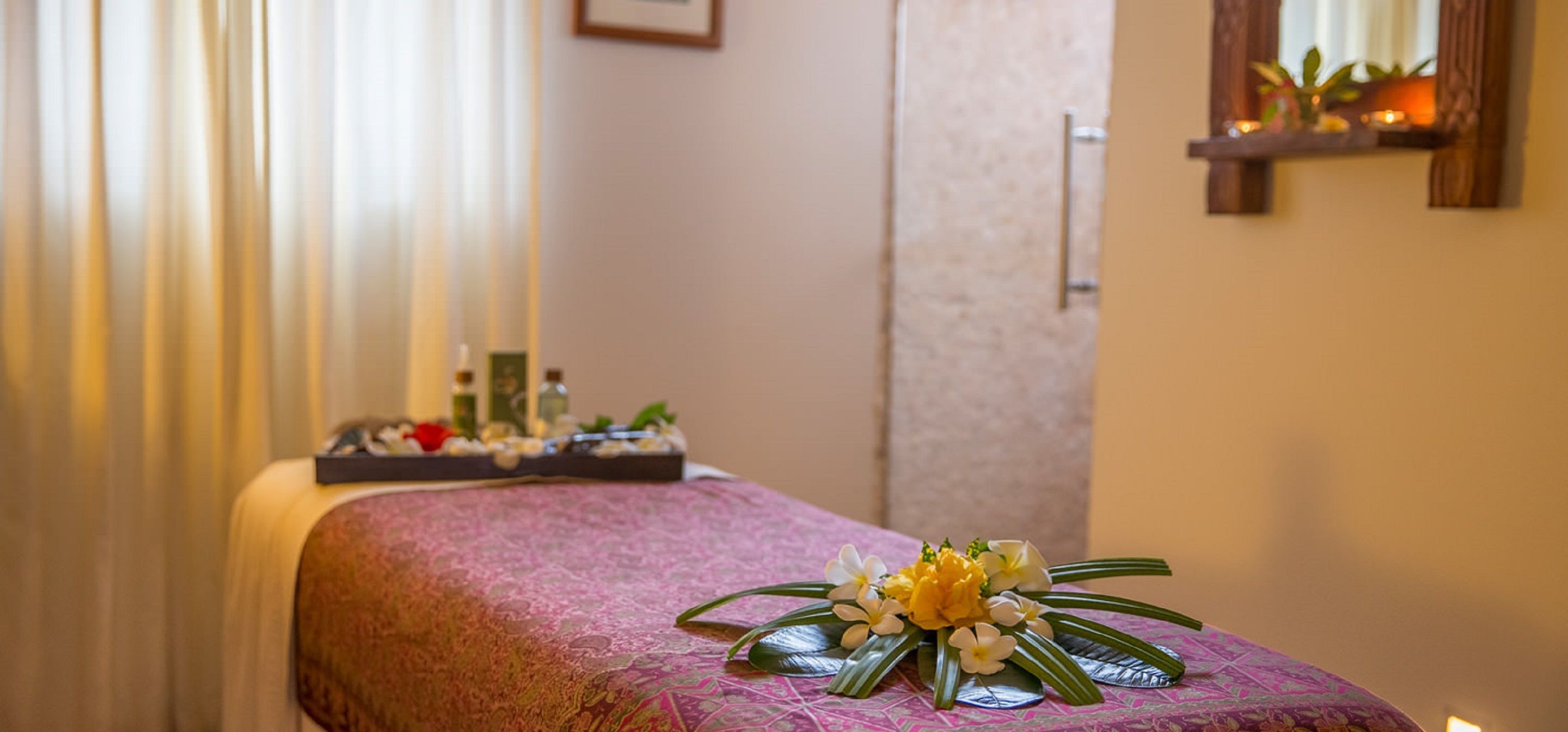 Uma mesa de massagem com uma arrumação floral decorativa e uma bandeja com produtos de spa.