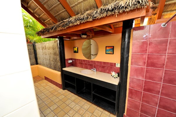 A bathroom with a thatched roof, a sink, a mirror, and red-tiled walls. - Bali Hai Resort & Spa (Cable Beach)