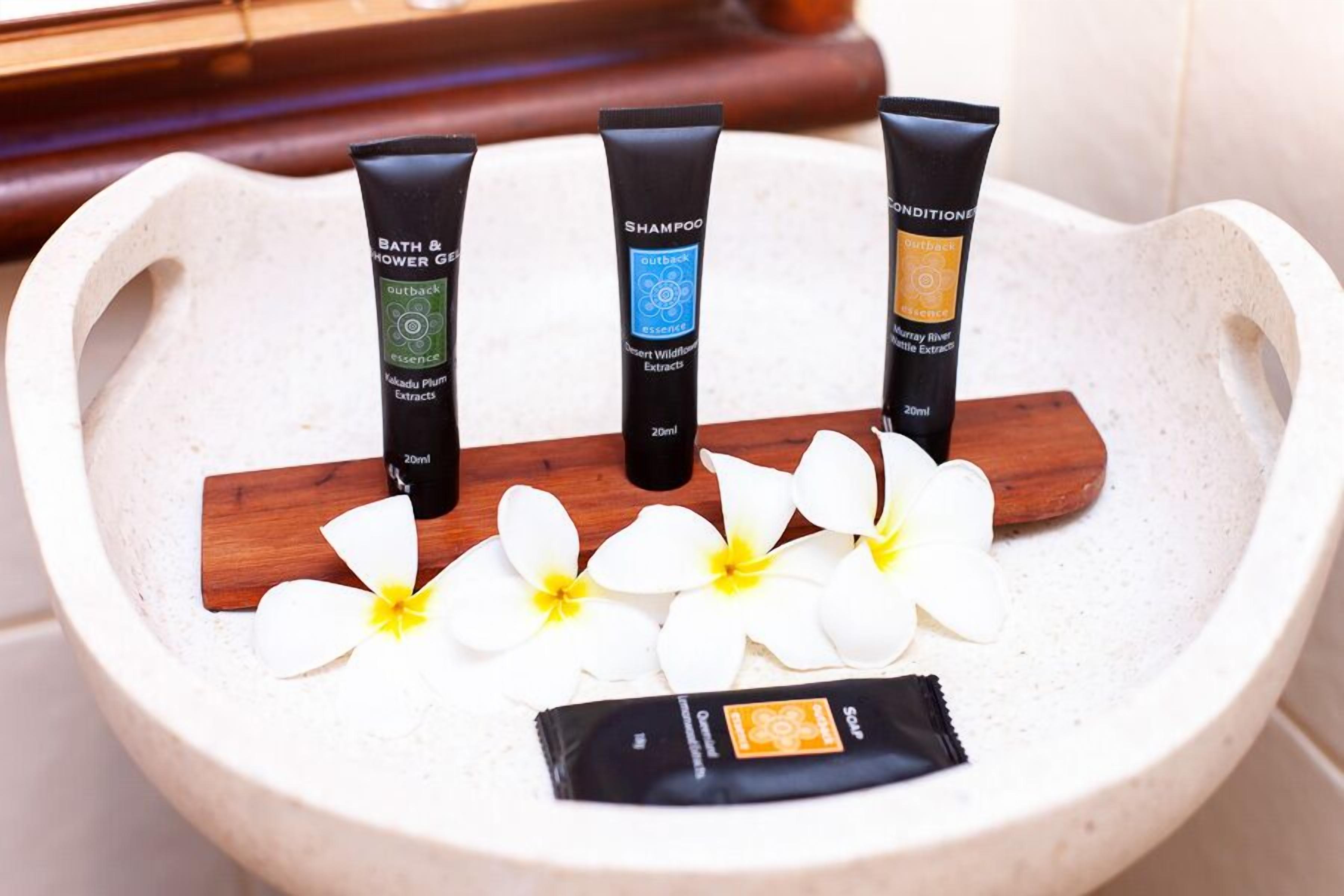 A stone basin with three tubes of bath and shower gel, a wooden stick, and white flowers.