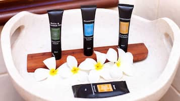 A stone basin with three tubes of bath and shower gel, a wooden stick, and white flowers.
