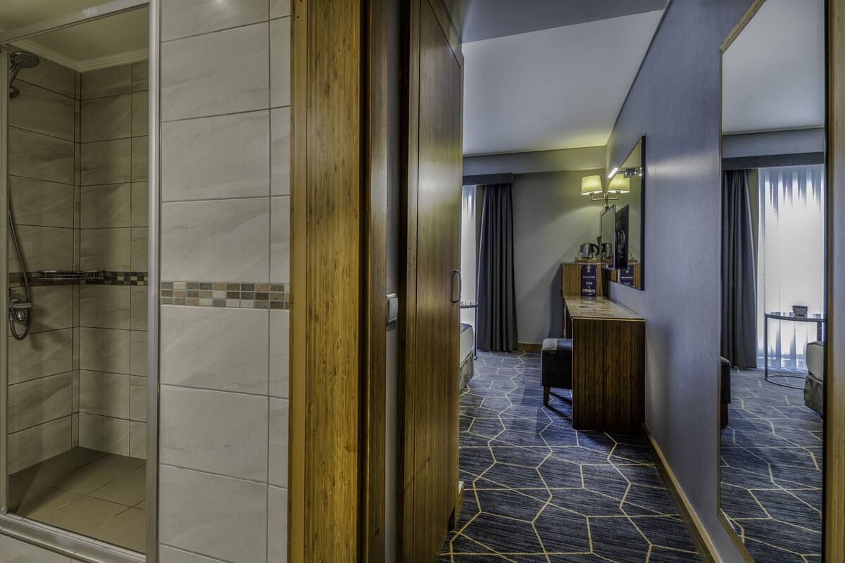 A hotel bathroom with a shower, a vanity with a mirror, and a seating area with a table and chairs.
