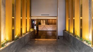 Un vestíbulo de hotel con mostrador de recepción de mármol, arcos de madera y una lámpara de araña moderna.