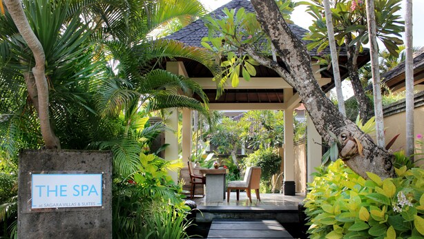 Entrada de um spa com placa de pedra, degraus de madeira e exuberante vegetação tropical.