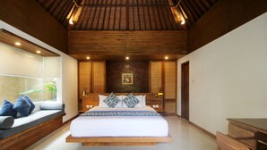 Um quarto espaçoso com uma cama grande, um banco embutido com almofadas, uma escrivaninha de madeira e uma janela ampla com vista para o verde.