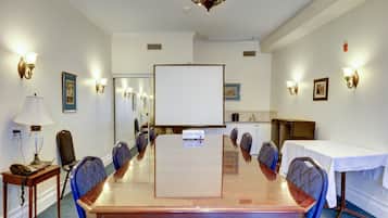 Ein Konferenzraum mit langem Tisch, Stühlen, einer Projektionsleinwand und Wandleuchten.