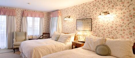 Un dormitorio con dos camas, una silla, una mesita de noche y papel tapiz con motivos florales.