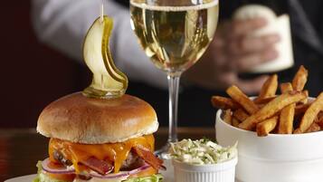 A burger with pickles, a glass of white wine, and a bowl of fries on a plate.
