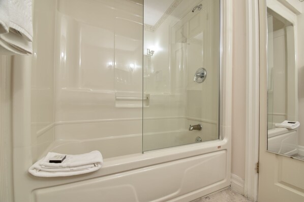 A modern bathroom with a glass-enclosed shower, a white bathtub, and a mirror reflecting the room. - The Waring House (Prince Edward)