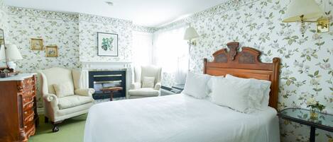 A bedroom with a large bed, two chairs, a dresser, and a fireplace.