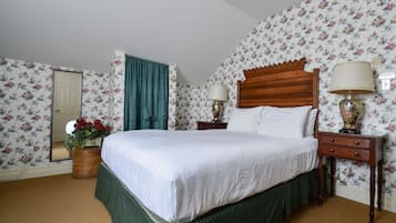 Een keurig opgemaakt bed met een houten hoofdbord, een nachtkastje met een lamp, en een behang met een bloemenmotief.