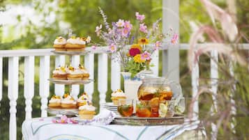 A tiered dessert stand with cupcakes and a pitcher of iced tea on a table outdoors.